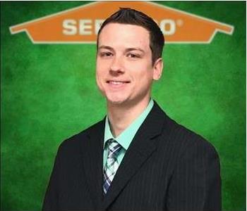 Male employee smiling in front of SERVPRO logo
